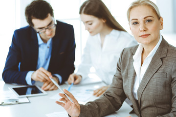 Headshot of business woman at negotiation. Group of business people discussing questions at meeting in modern office. Teamwork, partnership and business concept