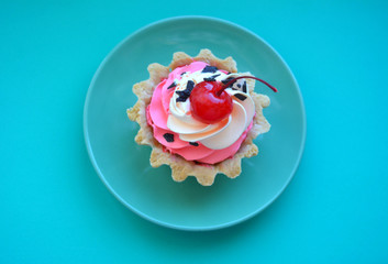 Beautiful cake with red cherry berries and cream on a plate on a blue background. Flat lay. Top view. Copy space.