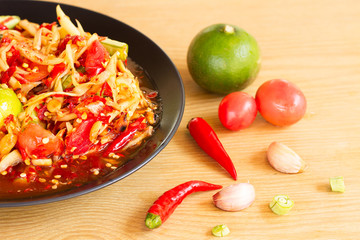 Som Tam or Spicy Papaya Salad In a black plate on a wooden table.