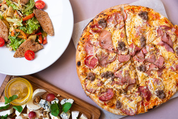 Dining table with food, top view. Pizza, salad, cheese board. Close-up.