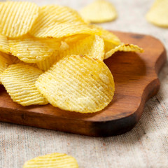 Salted wavy potato chips on a rustic wooden board, low angle view. Closeup.