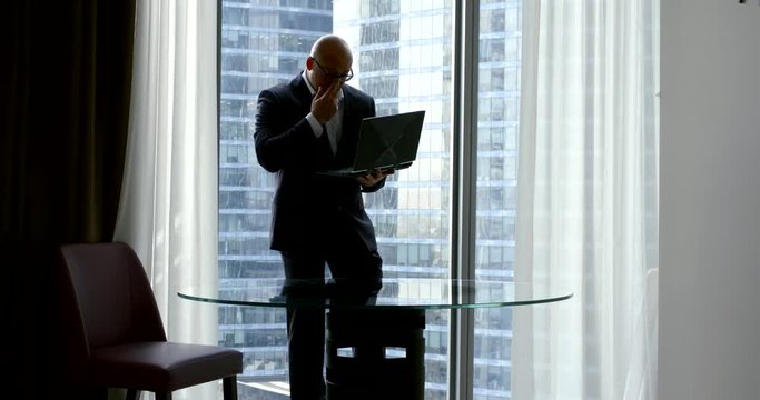 male lawyer is working in his office, standing near window and holding open laptop in hands