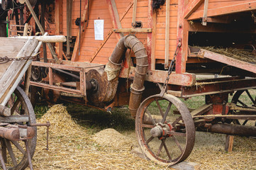 Historische Dreschmaschine in Betrieb. Im Vordergrund steht ein historischer Wagen aus Holz für den gemähten Weizen