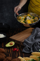 A person serving chicken soup with potato and corn