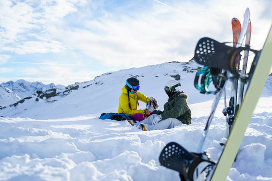 Image of ski, snowboard, ski poles on the background of two tourists with thermos in hands sitting on snow resort.