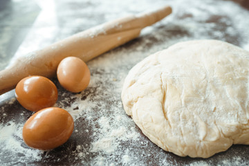 Dough, rolling pin, egg and flour on wooden table. Raw pizza dough with ingredients on the kitchen table. Dark background. Сooking concept.