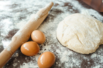Dough, rolling pin, egg and flour on wooden table. Raw pizza dough with ingredients on the kitchen table. Dark background. Сooking concept.