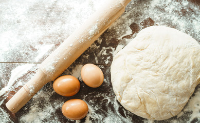 Dough, rolling pin, egg and flour on wooden table. Raw pizza dough with ingredients on the kitchen table. Dark background. Сooking concept.