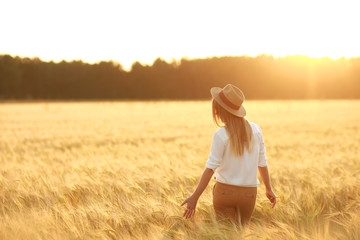 A girl in a hat stands in a wheat field at sunset © ranji