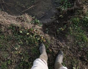 Adult standing next to a riverbank, wearing wellington boots.