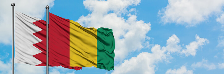Obraz premium Bahrain and Guinea flag waving in the wind against white cloudy blue sky together. Diplomacy concept, international relations.