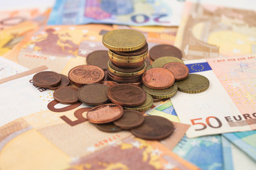 A pile of euro coins scattered on fifty and twenty euros euro bills