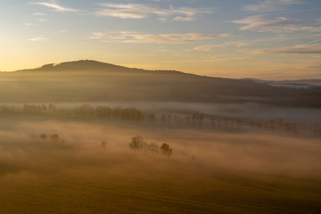 Aerial view to trees silhouette in misty orange fog at sunrise, Czech landscape