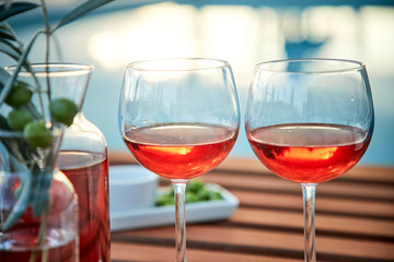 two glasses of rose wine with  olives against blue water on a pier..