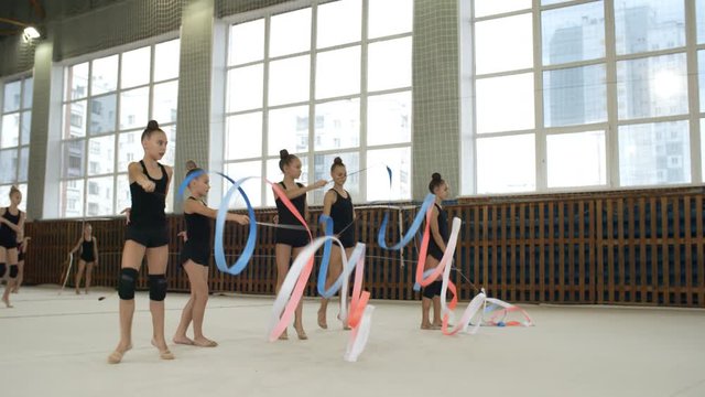 Group of teenage girls in sportswear dancing with ribbons while having rhythmic gymnastics class in school gym