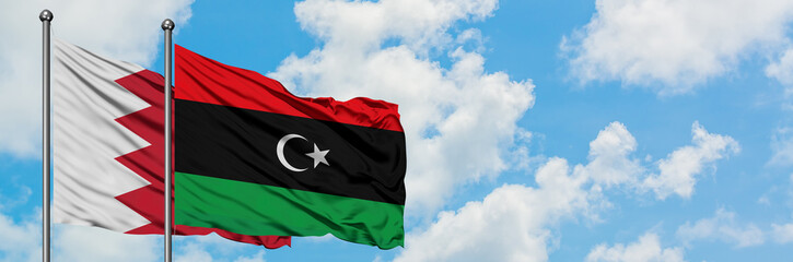 Bahrain and Libya flag waving in the wind against white cloudy blue sky together. Diplomacy...