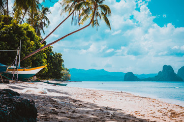 Banca boat on shore under palm trees.Tropical island scenic landscape. El-Nido, Palawan
