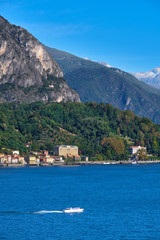 Fototapeta na wymiar Panoramic view of Lake Como. Lombardy, Italy. Boat in motion on the water. Autumn season. Perfect clear blue sky.
