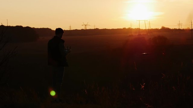 Young man controls a quadcopter in the countryside at sunset, drone takes pictures in the field