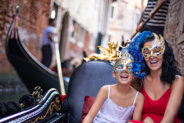 A mother and her daughter wears Venetian masks and traveling with gondola at the canals  of Venice, Italy 