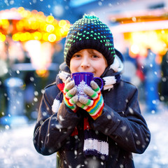 Little cute kid boy drinking hot children punch or chocolate on German Christmas market. Happy child on traditional family market in Germany, Laughing boy in colorful winter clothes