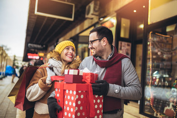 Young couple dressed in winter clothing holding gift boxes outdoor.