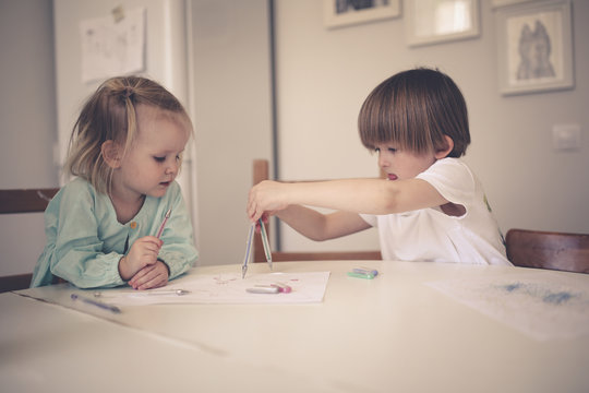 siblings together draw at table in bright kitchen