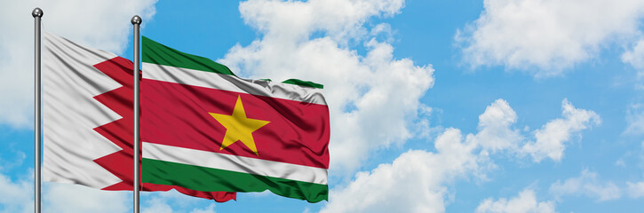 Obraz premium Bahrain and Suriname flag waving in the wind against white cloudy blue sky together. Diplomacy concept, international relations.