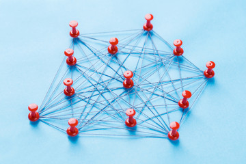 network with red pins and string, An arrangement of colorful pins linked together with string on a blue background suggesting a network of connections.