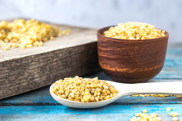 Dry bulgur grain in a wooden spoon. Healthy, dietary, vegan, gluten free product.