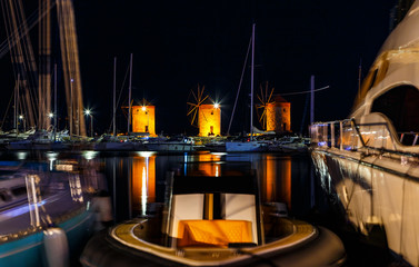 The famous mills of island of Rhodes on pier among stocks of yachts at night with beautiful lighting.
