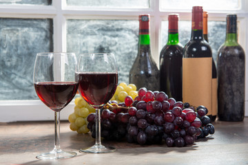 Composition with two wineglasses, grapes and bottles of red wine