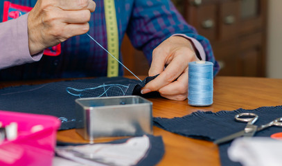 Detail of hands of senior female seamstress sewing cloth to make a garment in her workshop