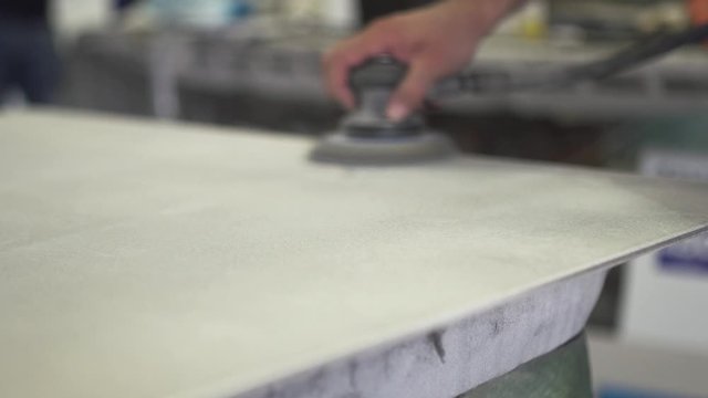 Worker using a handheld power tool to polish a metallic surface. Man is moving hand from left to right and up and down. Slow motion. 