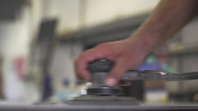 Close up of a man holding a hand tool. Worker is smoothing a metal workpiece surface. View from the inside of a metal factory. Slow motion.