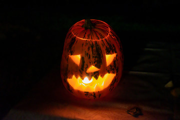 Carved halloween pumpkin lantern with burning candle inside at night.