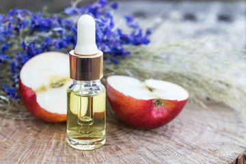 Bottle of apple essential oil and fresh apples on a wooden table. Essential oil is used to fill lamps, perfumes and in cosmetics.