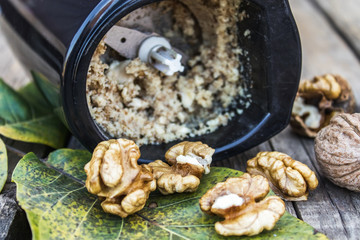 chopped walnut in a coffee grinder near the walnut kernel on an old wooden table.