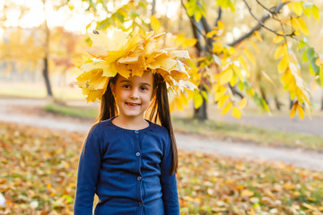 Portrait of smiling child with wreath of leaves on head. Background of sunny autumn park.