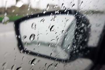 Raindrops on the glass and on the rearview mirror of the car. Dangerous driving in bad weather. Selective focus.