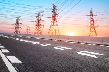 Fototapeta na wymiar Electricity tower silhouette and empty asphalt road at dusk