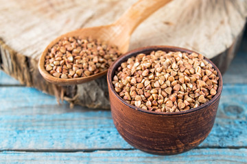 Uncooked buckwheat in a bowl on old blue boards. Buckwheat is used for cooking.