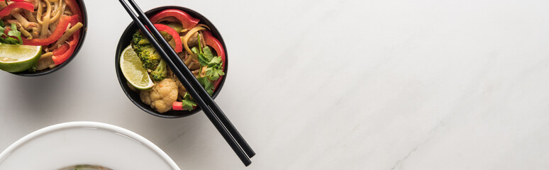 top view of delicious meat and vegetable thai noodles with chopsticks on marble grey surface, panoramic shot