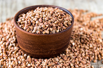 Uncooked buckwheat in a bowl on old boards. Buckwheat is used for cooking.
