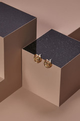 Object photo of a golden mother-of-pearl heart earrings, located on a dark beige cube with black...