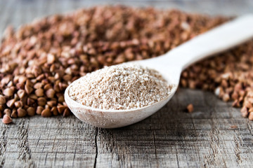 Buckwheat flour in a wooden spoon on a pile of roasted buckwheat. A pile of buckwheat flour.