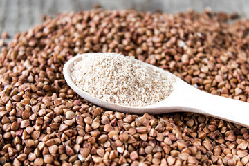 Buckwheat flour in a wooden spoon on a pile of roasted buckwheat. A pile of buckwheat flour.