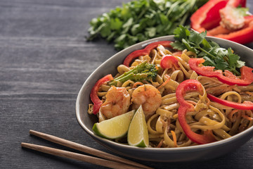 delicious spicy thai noodles with shrimps near chopsticks on wooden grey surface