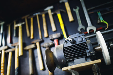 grinding machine in old garage, wall with rusty hammers background