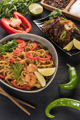 tasty spicy thai noodles near chopsticks and ingredients on wooden grey surface
